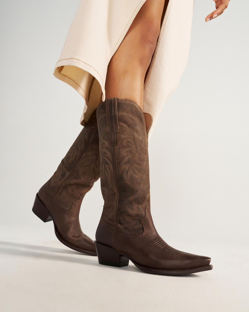 The Annie in Cafe Goat. A person wearing a cream-colored skirt and dark brown cowboy boots stands on a light surface, capturing the cozy charm of Cafe Goat.