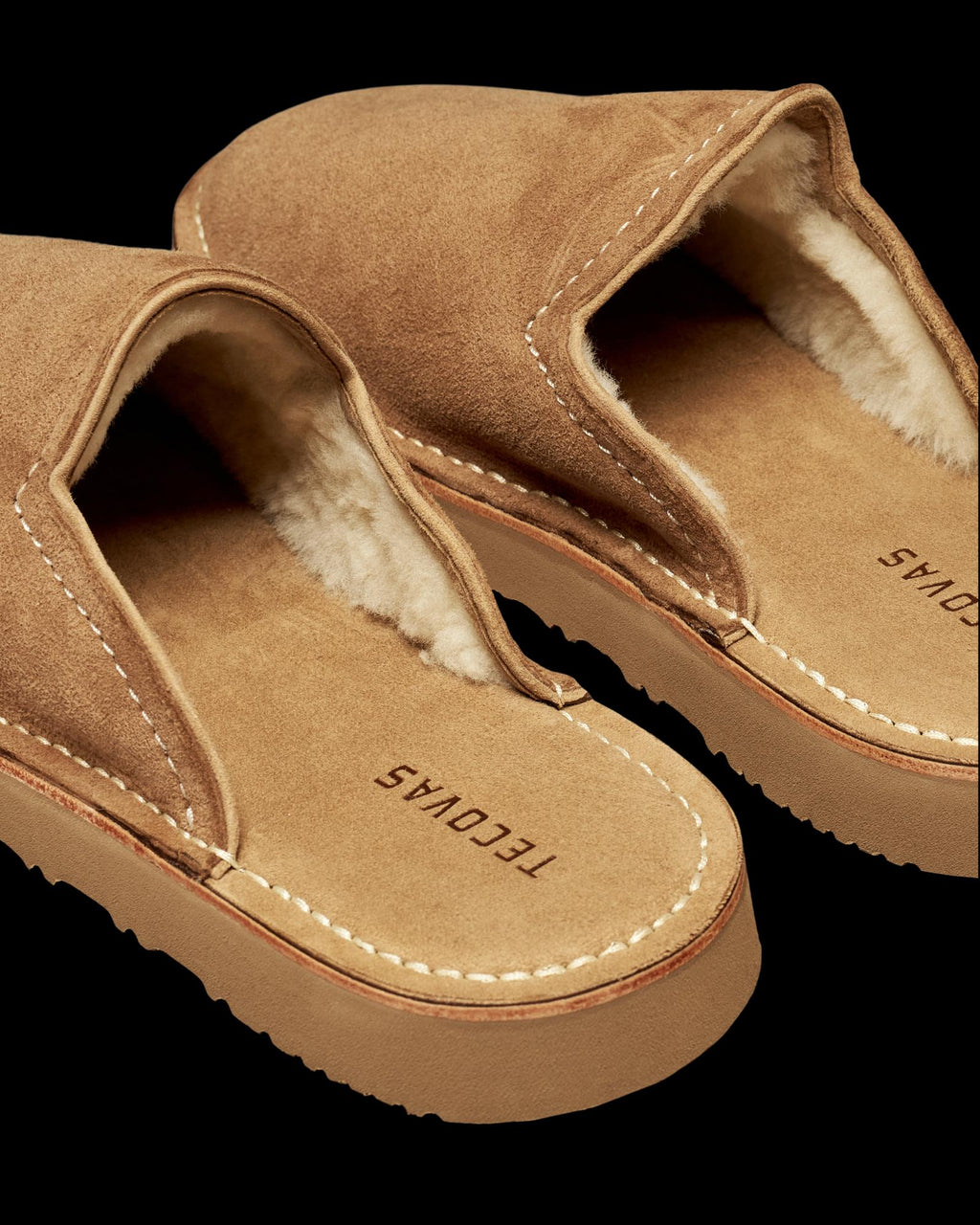 The Oliver in Cognac Suede with Shearling. Pair of cognac suede slip-on slippers with shearling lining and Tecovas branding on the footbed.