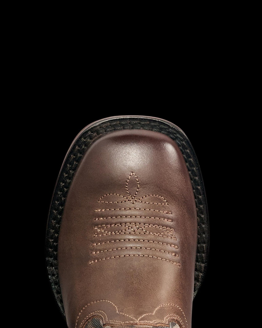 Close-up of a brown leather boot with decorative stitching on the square toe and a black textured outsole, viewed from above.