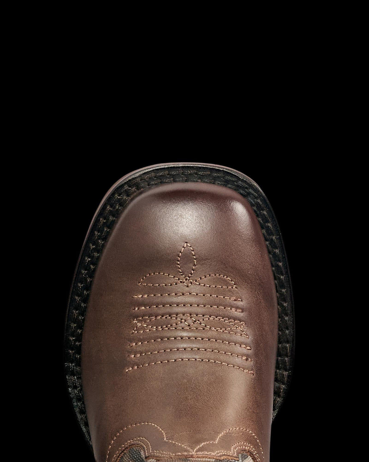 Close-up of a brown leather boot with decorative stitching on the square toe and a black textured outsole, viewed from above.