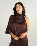 Woman with long dark hair wearing a shiny, dark brown, asymmetrical dress with fringe detail, posing against a plain light background.