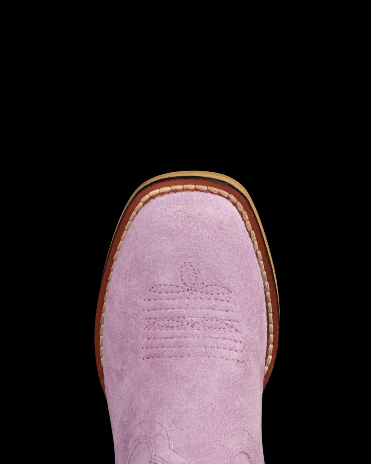 Close-up of the toe of a pink suede cowboy boot with decorative stitching, visible brown sole, and white welt stitching.
