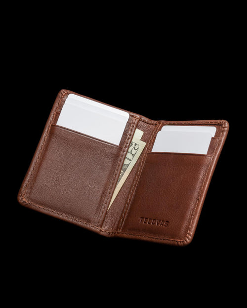 Open brown leather wallet with card slots and visible cash, embossed with the word "Tecovas" on the right side.