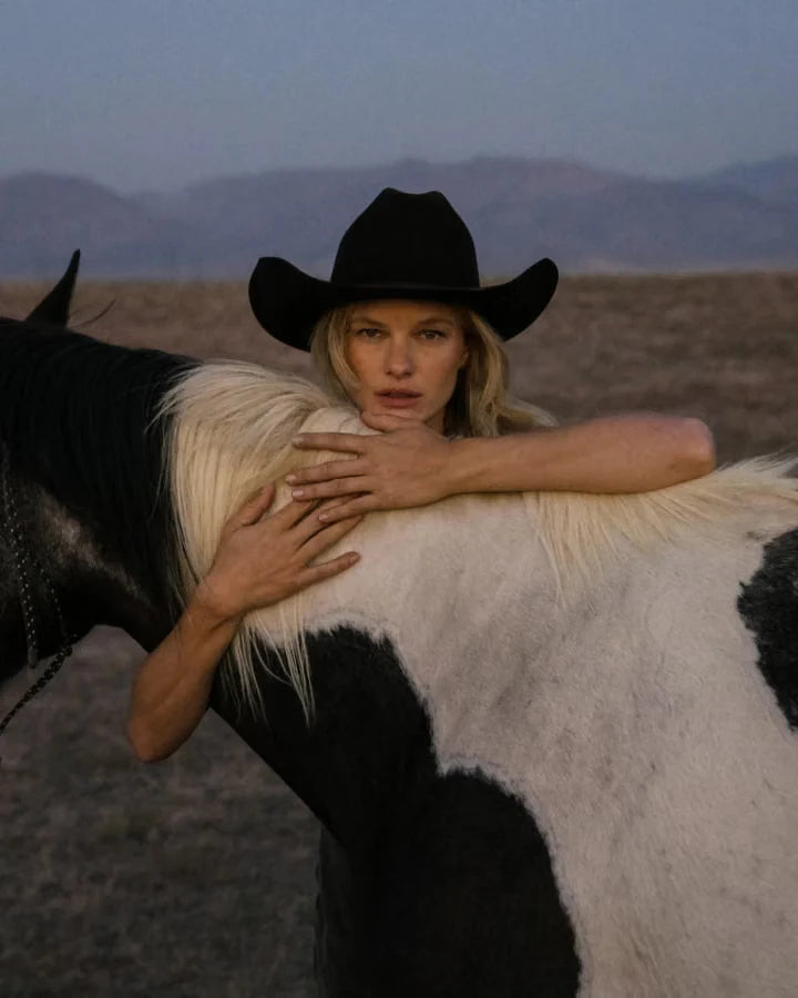 A woman wearing a black hat beside a horse